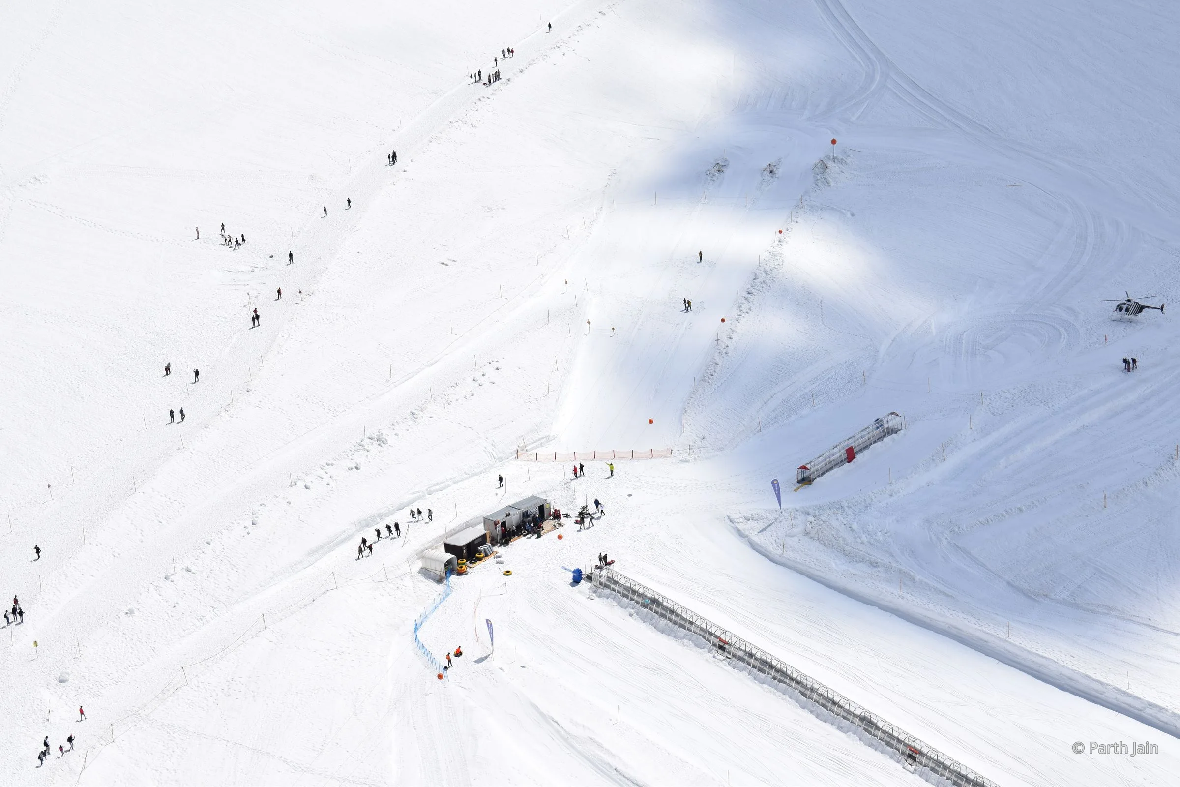 A small rescue helicopter crossing a vast snowfield, seen from above.
